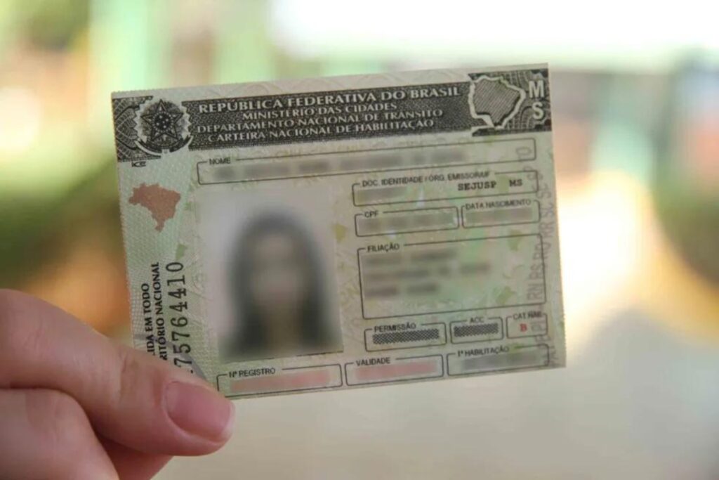 Mão segurando uma carteira de motorista brasileira.