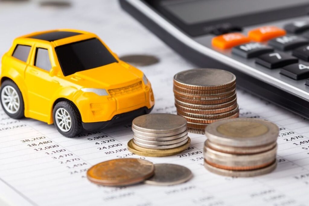 Carro miniatura, moedas e calculadora em documentos financeiros.